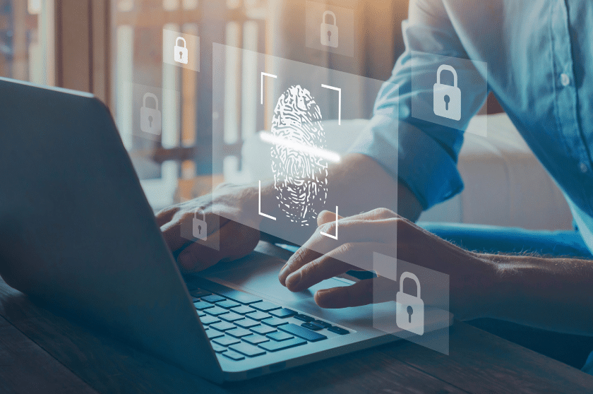 A person typing on a laptop with a digital fingerprint and padlock icons floating above, symbolizing digital security and authentication technology. Sunlight streams in from a window in the background.