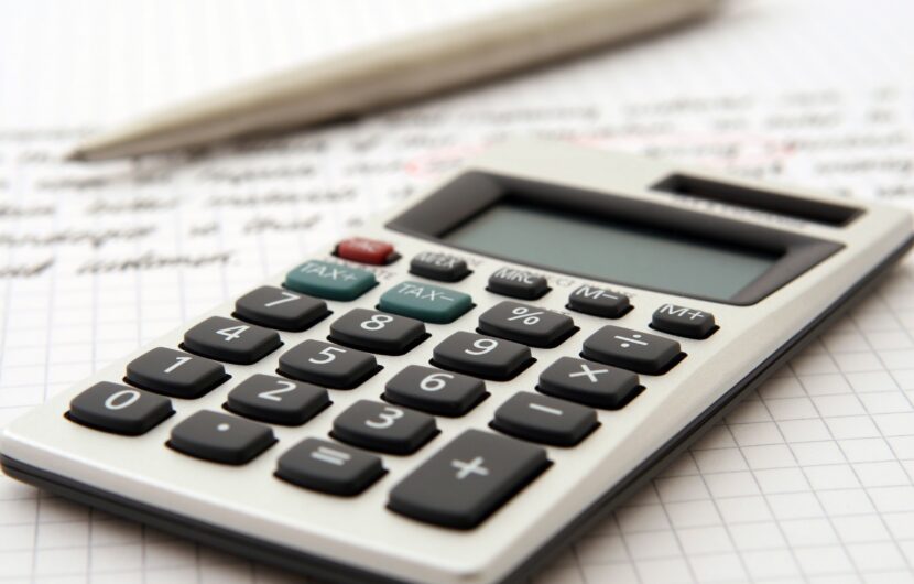 A calculator rests on a notebook with graph paper. A pen is placed in the background. The scene suggests a work or study setting focused on calculations or analysis.