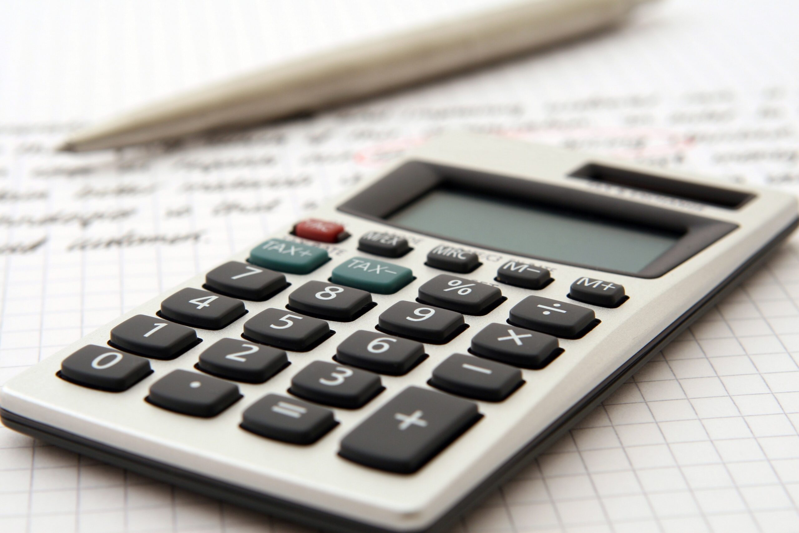 A calculator rests on a notebook with graph paper. A pen is placed in the background. The scene suggests a work or study setting focused on calculations or analysis.