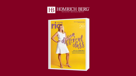 A woman in a white dress stands confidently on the cover of a yellow magazine. The text reads, A Different Class. The logo of Homrich Berg Wealth Management is displayed above the magazine on a red background.