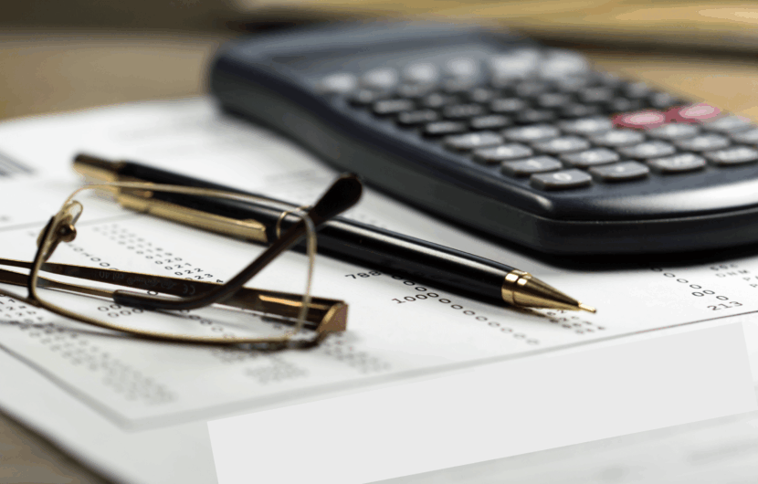 A close-up image of a calculator, a pair of glasses, and a pen placed on a paper with printed numbers. The focus is on the workspace essentials, suggesting financial or mathematical work in progress.