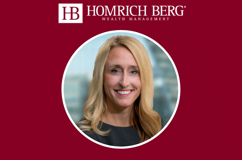 A woman with long blonde hair is smiling. She is wearing a black top. The background is maroon with the text Homrich Berg Wealth Management and a logo above the image.