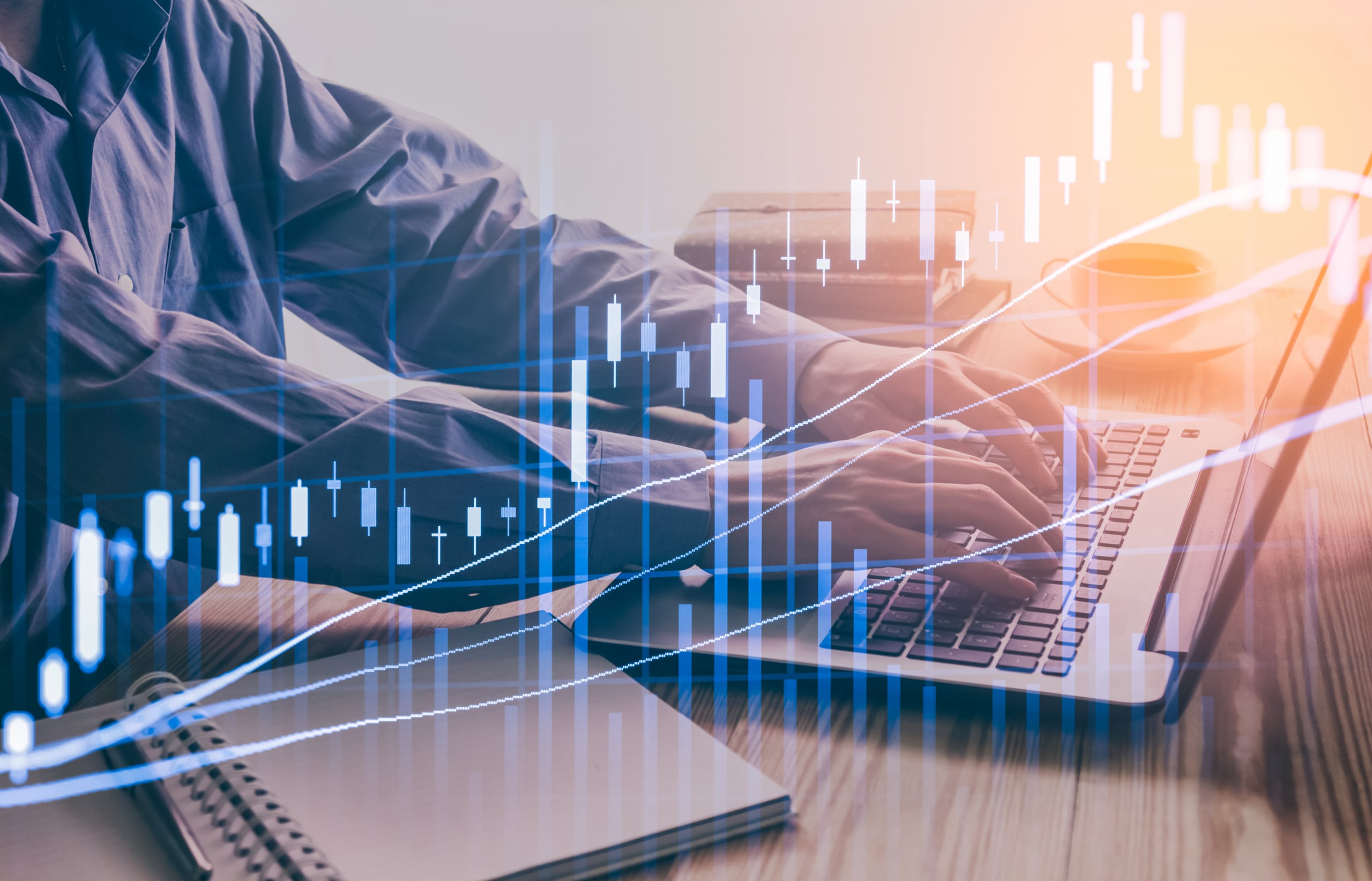 Person typing on a laptop with a digital stock market graph overlay. The graph features candlestick charts and rising lines, symbolizing financial analysis or trading. A notebook and a coffee cup are on the desk.