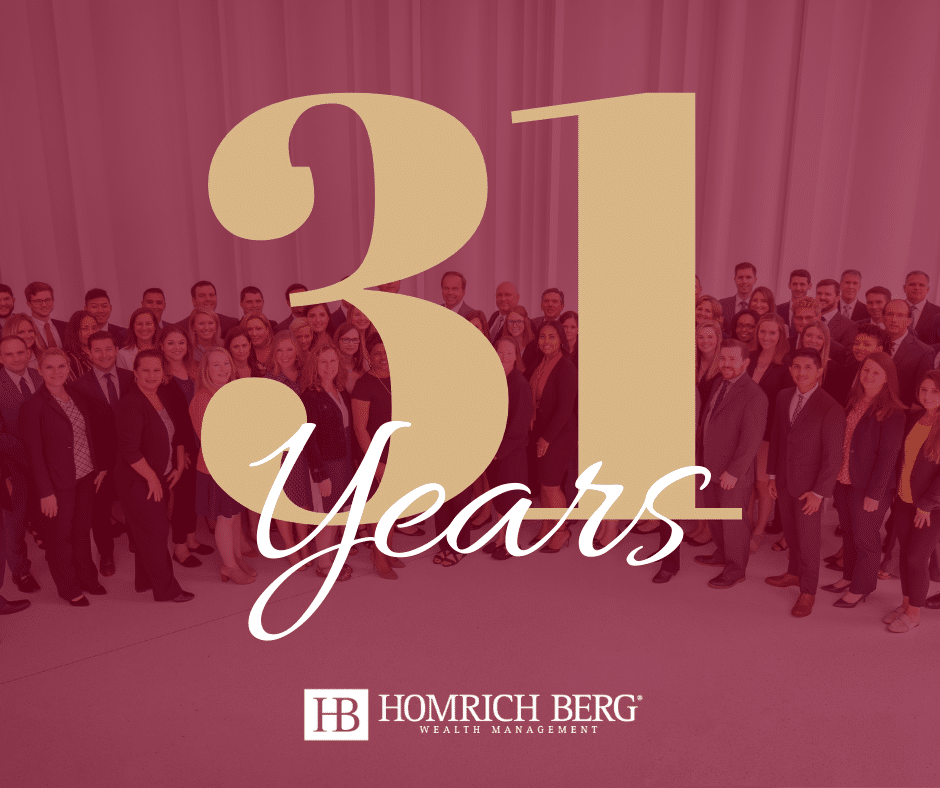 A large group of people stand together smiling in front of a backdrop displaying 31 Years in large letters. At the bottom, Homrich Berg Wealth Management is written with the companys logo.