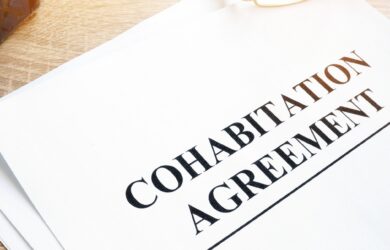 A document titled Cohabitation Agreement rests on a wooden surface. Nearby, a pair of glasses is partially visible, suggesting review or signing. The scene is well-lit, emphasizing the importance of the paperwork.