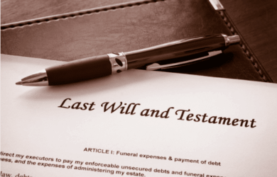 A pen rests on an official document titled Last Will and Testament, with a focus on Article I regarding funeral expenses and debt payment, placed on a dark surface.