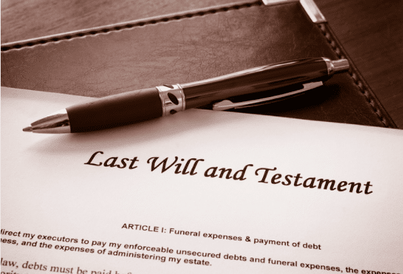 A pen rests on an official document titled Last Will and Testament, with a focus on Article I regarding funeral expenses and debt payment, placed on a dark surface.