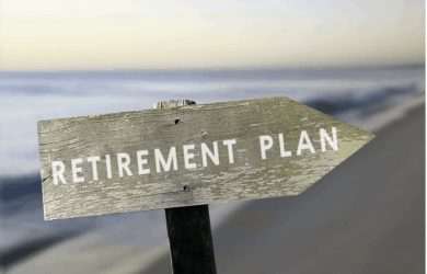 A weathered wooden sign with the text RETIREMENT PLAN points toward a blurred beach landscape in the background, indicating a connection between retirement and a relaxing seaside environment.