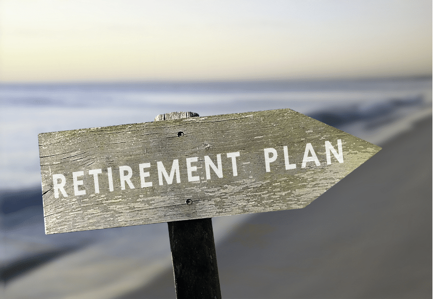 A weathered wooden sign with the text RETIREMENT PLAN points toward a blurred beach landscape in the background, indicating a connection between retirement and a relaxing seaside environment.