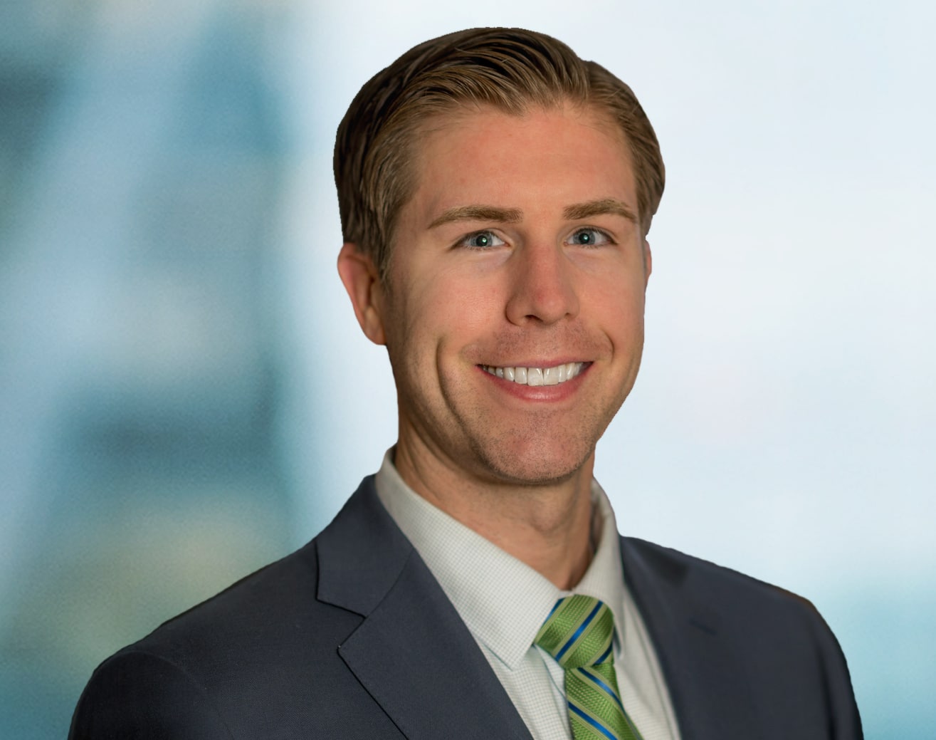 A smiling man in a suit with a green and white striped tie stands against a blurred blue background.
