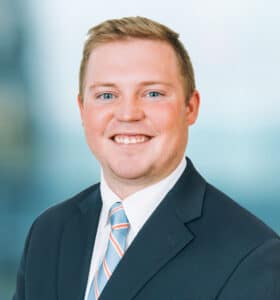 A smiling man in a business suit and striped tie poses against a blurred background.