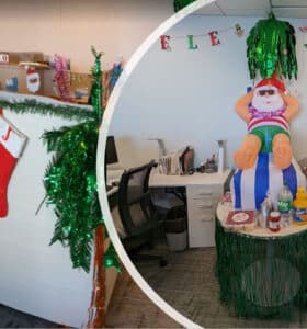 An office decorated for Christmas with stockings on desks and a tropical theme. A stuffed figure in sunglasses and swimwear sits on a barrel surrounded by tropical decorations and a banner reading Mele Kalikimaka.