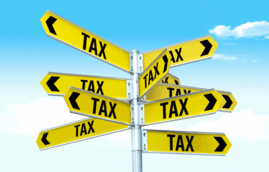 A signpost with multiple yellow arrows pointing in different directions, each labeled with the word TAX in bold black letters, set against a blue sky with some clouds.
