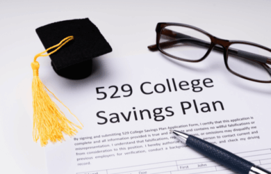 Image of a 529 College Savings Plan application form on a table. A miniature graduation cap and a pair of glasses are placed above the form, which is partially visible. A pen rests on the form, suggesting its ready to be filled out.