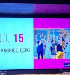 A group of people posing and smiling in a celebratory manner. The display indicates Homrich Berg Wealth Management is ranked No. 15 among best places to work, as presented by the Atlanta Business Chronicle.