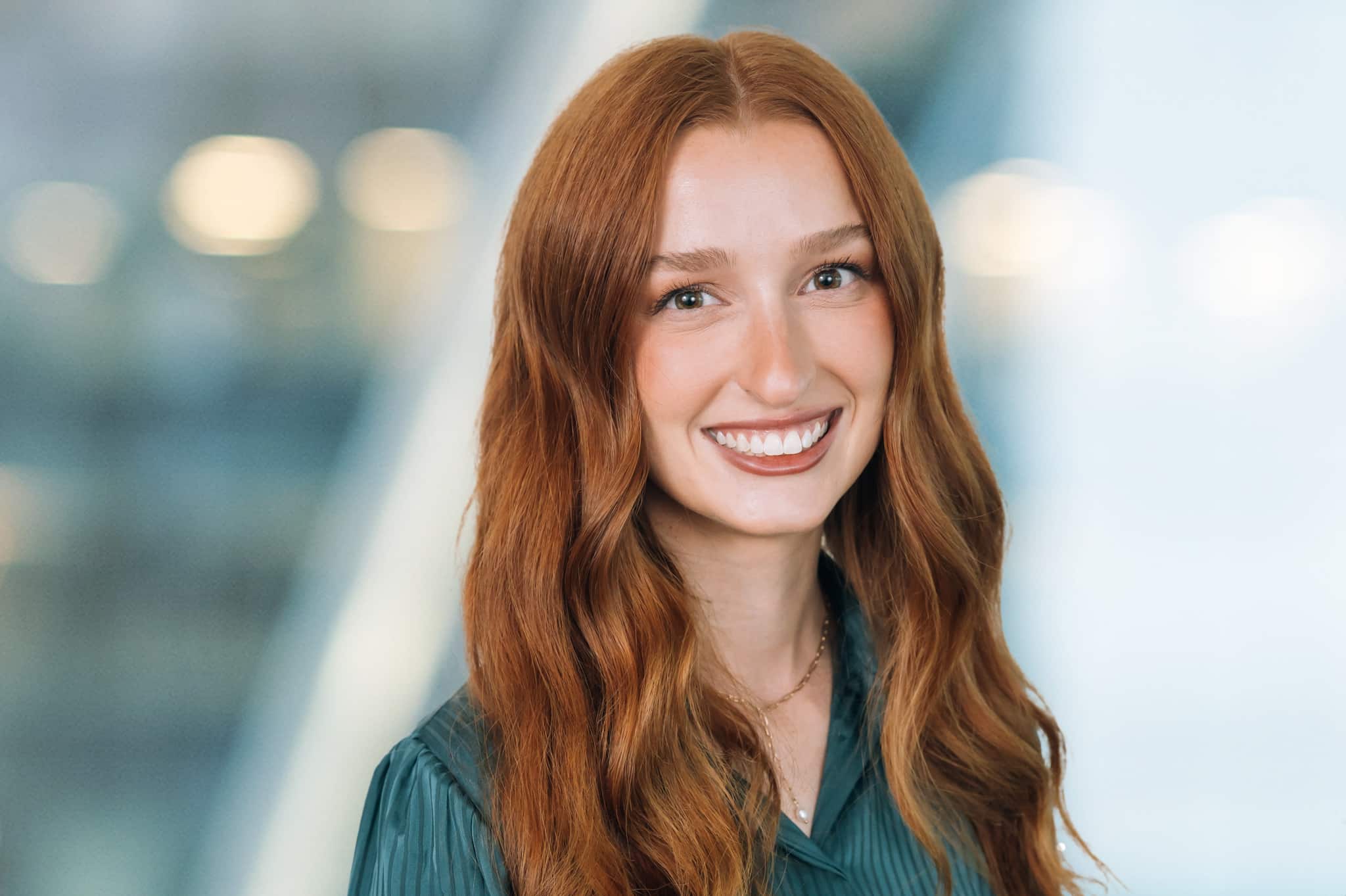 A person with long red hair and a green top smiles against a blurred background.