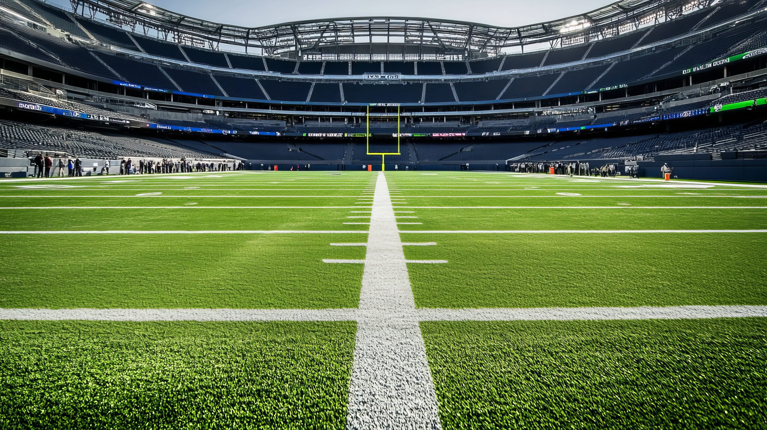A view from midfield looking toward the end zone in an empty football stadium, with bright green turf and white yard lines under a clear sky.
