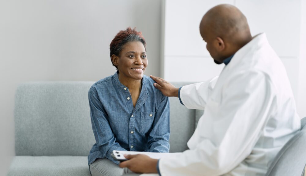 A man in a white coat touching a womans shoulder.