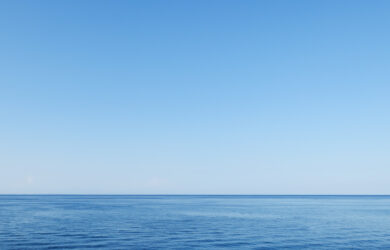 A calm, blue ocean stretches to the horizon under a clear, cloudless sky, creating a peaceful and serene seascape.