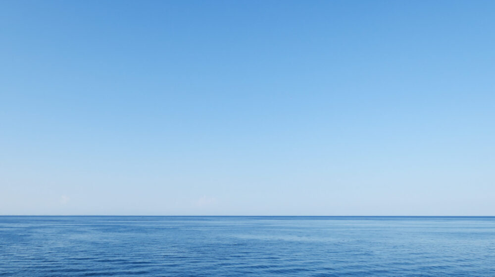 A calm, blue ocean stretches to the horizon under a clear, cloudless sky, creating a peaceful and serene seascape.