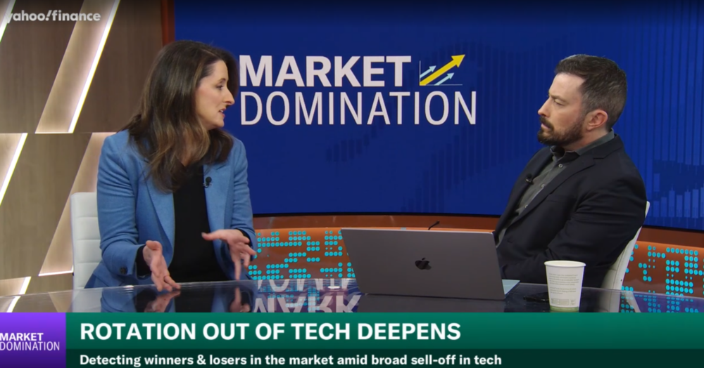 Two people sit at a news desk discussing Rotation Out of Tech Deepens on Yahoo Finances Market Domination, with a blue background and a laptop and coffee cup on the table.
