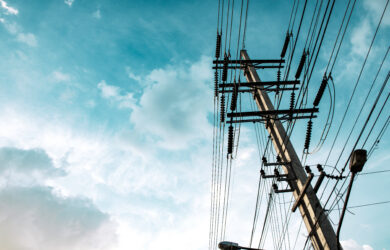 A utility pole with multiple power lines extending outward, set against a blue sky with scattered clouds.
