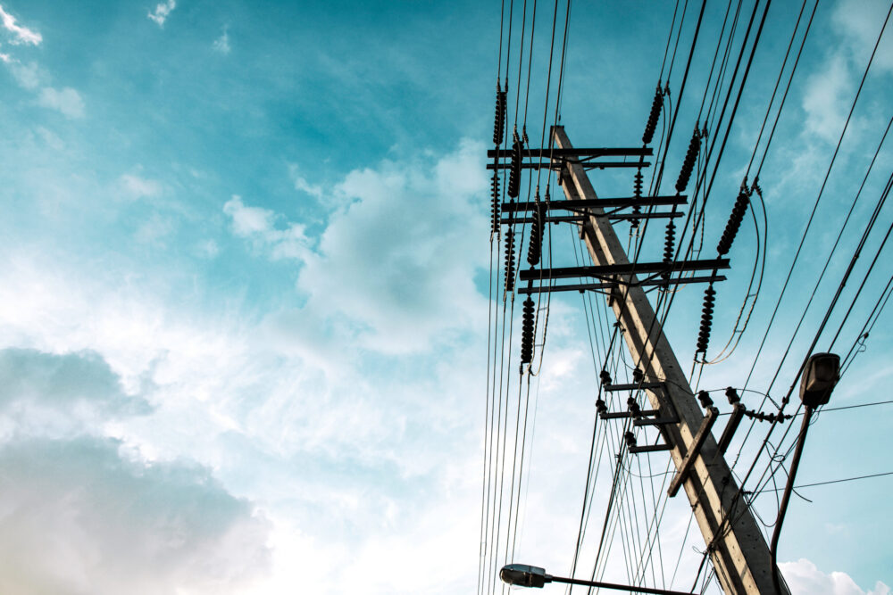 A utility pole with multiple power lines extending outward, set against a blue sky with scattered clouds.