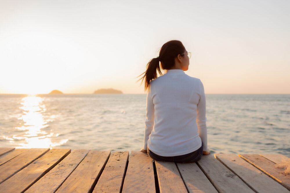 Lonely woman sitting on a wooden bridge sunset.are Lonely. during the time Sunset in winter