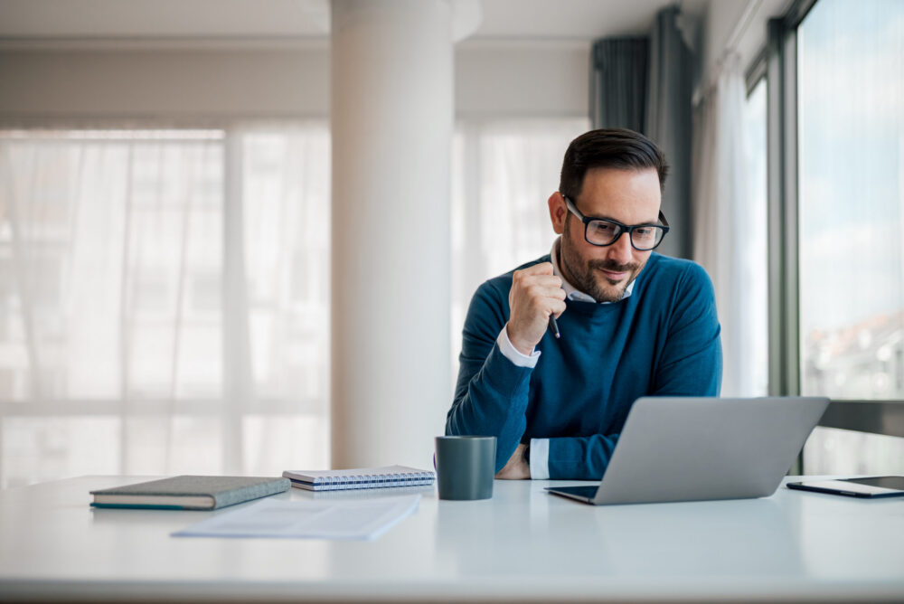 Serious businessman working on laptop. Male professional is planning strategy while sitting at office desk. He is wearing formals in corporate workplace.