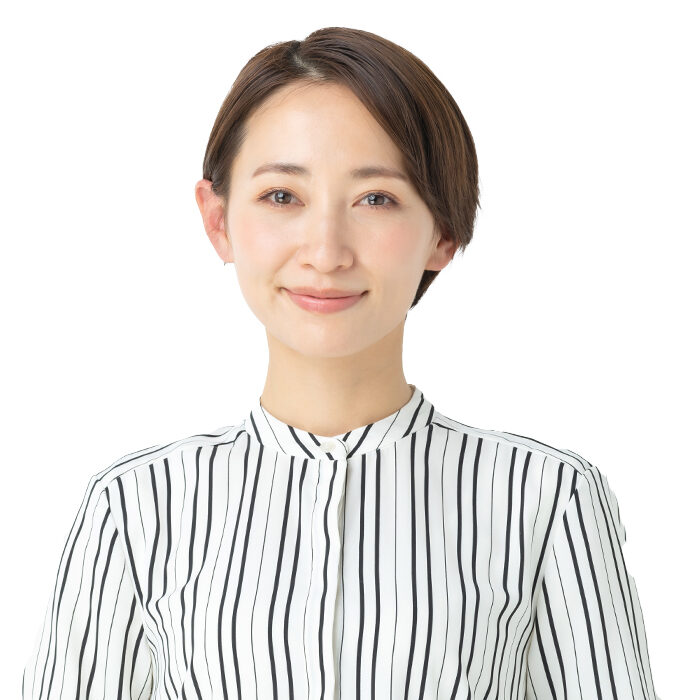 A person with short brown hair wearing a white shirt with black vertical stripes is smiling softly, standing against a plain white background.