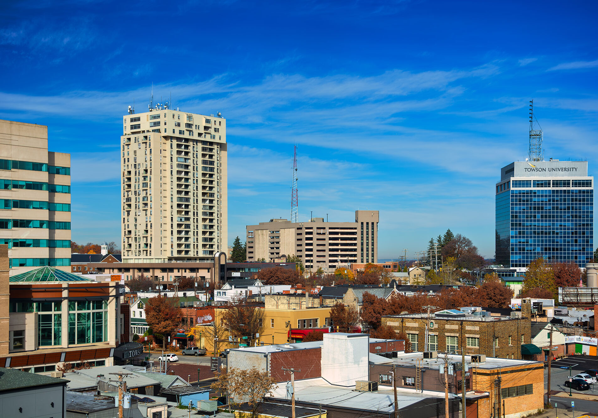 iStock-2149713087 A cityscape with mid-rise buildings, including one labeled “Toronto University,” surrounded by smaller structures and autumn trees under a clear blue sky.